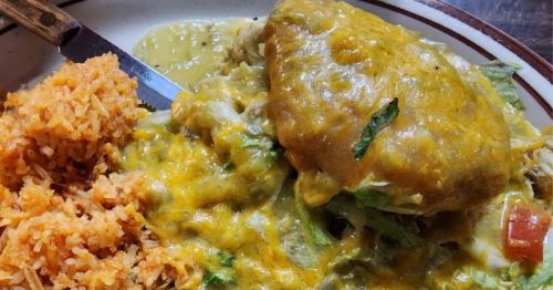 A plate of enchiladas topped with cheese and green sauce, served with a side of orange rice.