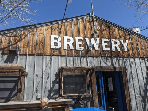 Exterior of a brewery with a wooden and metal facade, featuring large letters spelling "BREWERY" against a clear blue sky.