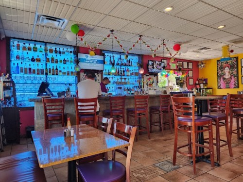 A vibrant bar area with colorful decor, shelves of liquor, and a patron sitting at the counter.