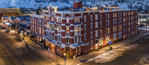 Historic brick hotel with ornate architecture, illuminated at night, surrounded by snow-covered streets and mountains.