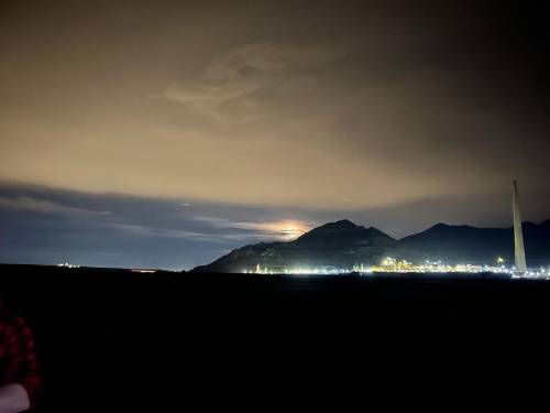 A nighttime landscape featuring a mountain silhouette, a glowing moon, and distant city lights under a cloudy sky.