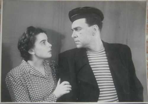 A black-and-white photo of a man in a striped shirt and hat, gazing intensely at a woman in a polka dot dress.