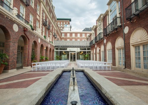 A courtyard with a water feature, lined with chairs for an event, surrounded by brick buildings and greenery.