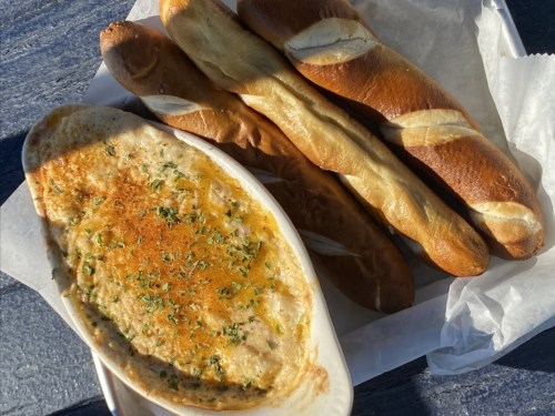A plate with creamy dip topped with herbs and several golden-brown breadsticks beside it.