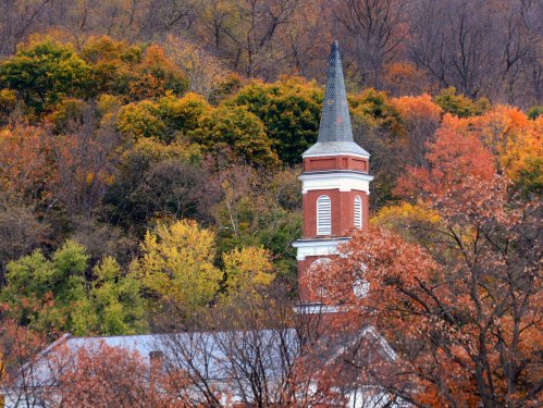 A church steeple rises above colorful autumn foliage on a hillside.
