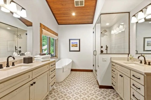 Modern bathroom featuring dual sinks, a freestanding tub, and stylish tile flooring. Natural light from a window.