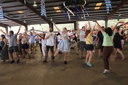 A lively crowd dances joyfully at a festive event, with colorful decorations and a cheerful atmosphere.
