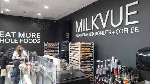 Interior of a donut shop named Milkvue, featuring displays of handcrafted donuts and a coffee station.