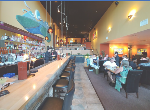 A spacious restaurant interior with a long bar, colorful decor, and diners enjoying their meals at tables.