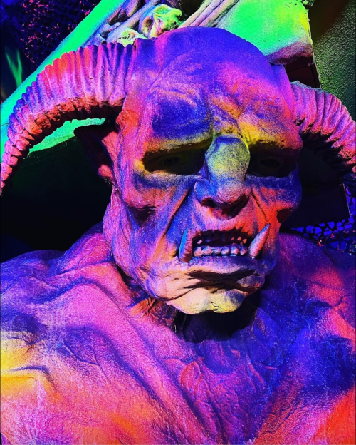 A colorful, monstrous figure with horns and a fierce expression, illuminated in vibrant hues.