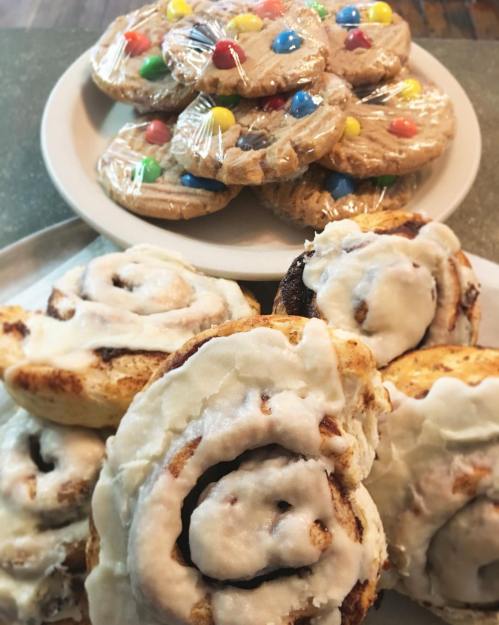 A plate of colorful cookies topped with candy, and a tray of frosted cinnamon rolls in the foreground.