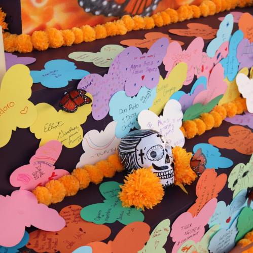 Colorful paper cutouts and messages adorn an altar, featuring a decorative skull and marigold flowers.