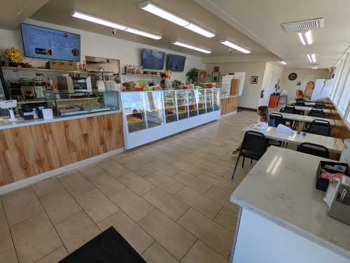 A bright café interior with display cases, tables, and a child sitting at a table, enjoying the space.