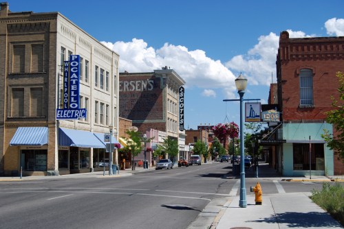 A sunny street view of downtown Pocatello, featuring historic buildings and storefronts under a blue sky with clouds.