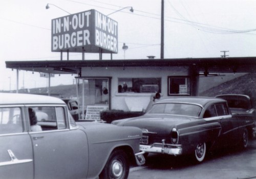 Black and white photo of an In-N-Out Burger drive-thru with classic cars parked outside.
