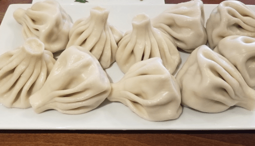 A plate of freshly made dumplings with a smooth, pleated surface, arranged neatly in a row.