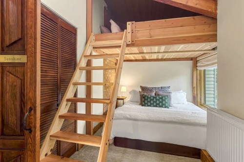 Cozy bedroom with a lofted bed, wooden stairs, and warm lighting, featuring a large bed and decorative pillows.