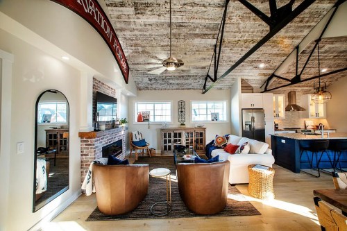 Cozy living space with a fireplace, modern furniture, and a kitchen area featuring exposed beams and natural light.