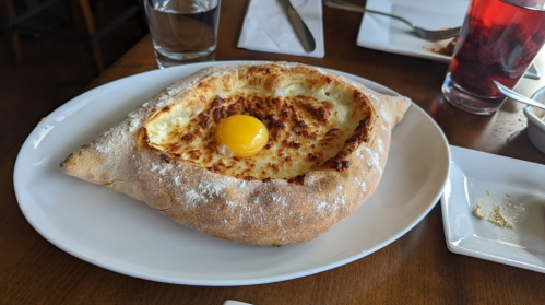 A round, baked bread dish filled with cheese and topped with a raw egg yolk, served on a white plate.