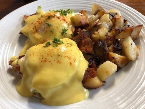 A plate of eggs Benedict topped with hollandaise sauce, served with crispy roasted potatoes.