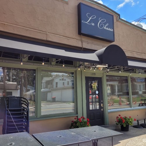Exterior of La Chasse restaurant with outdoor seating, a sign above, and a clear blue sky in the background.