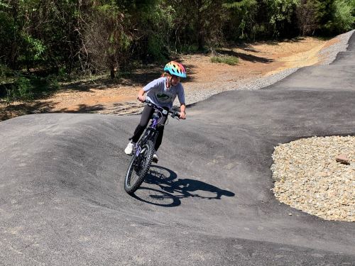 A child rides a bike on a winding path in a wooded area, wearing a helmet and enjoying the outdoors.