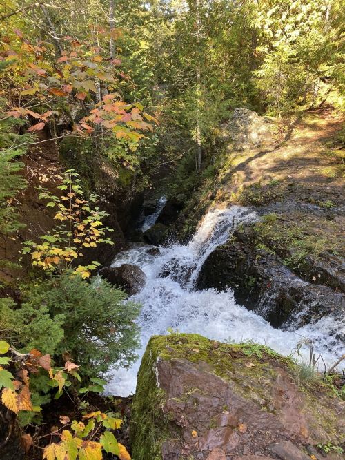 A serene waterfall cascades through a rocky landscape, surrounded by vibrant autumn foliage and lush greenery.