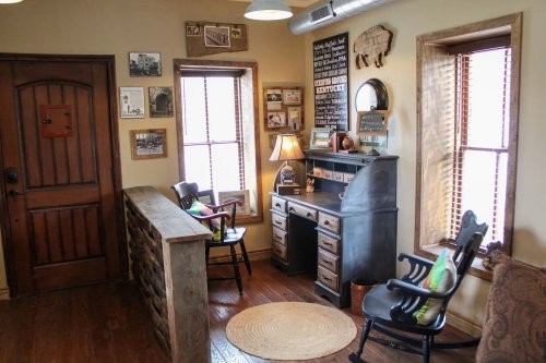 Cozy room with wooden furniture, a desk, rocking chair, and framed photos on the walls, illuminated by natural light.