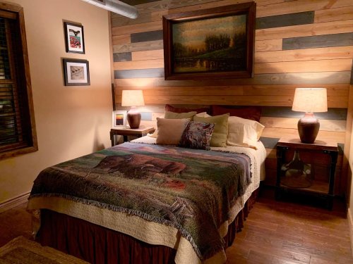 Cozy bedroom with a wooden accent wall, a bed with a colorful blanket, and warm lighting from bedside lamps.