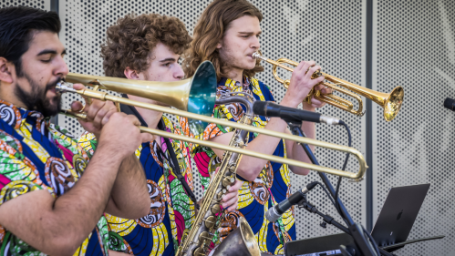 Three musicians in colorful shirts play brass instruments at a performance, focused on their music.