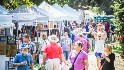 A bustling outdoor market with people browsing stalls and tents filled with various goods and crafts.