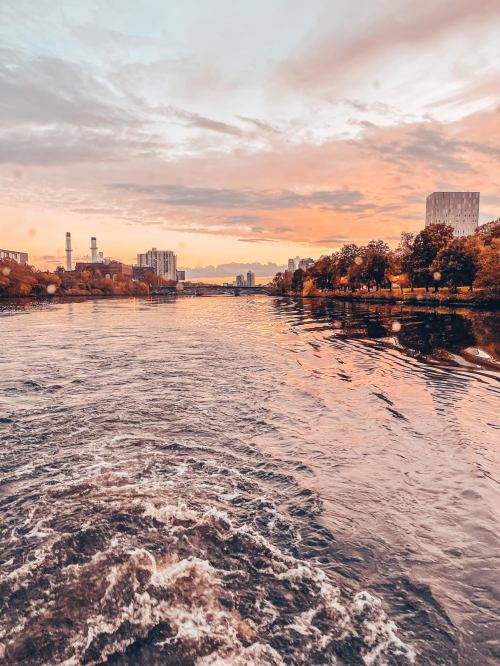 A serene river scene at sunset, reflecting colorful skies and city buildings along the banks.