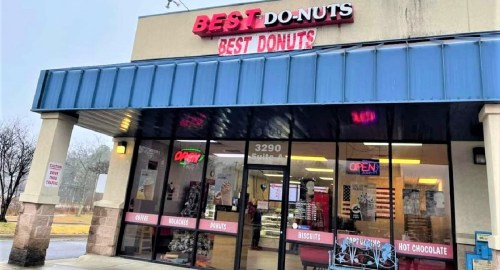 Exterior of "Best Do-Nuts" shop with a blue awning, open sign, and a variety of donuts displayed in the window.