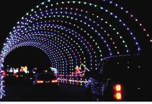 A colorful tunnel of lights with festive decorations, viewed from a car at night.