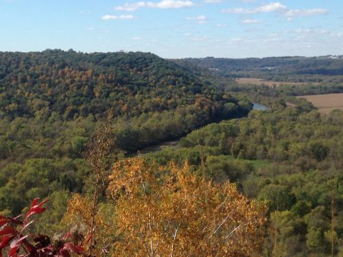 A scenic view of rolling hills with autumn foliage and a winding river below under a blue sky with scattered clouds.