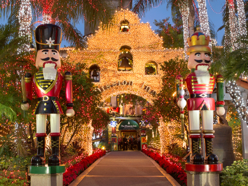 Two large nutcracker figures stand at the entrance of a beautifully lit building adorned with holiday lights.