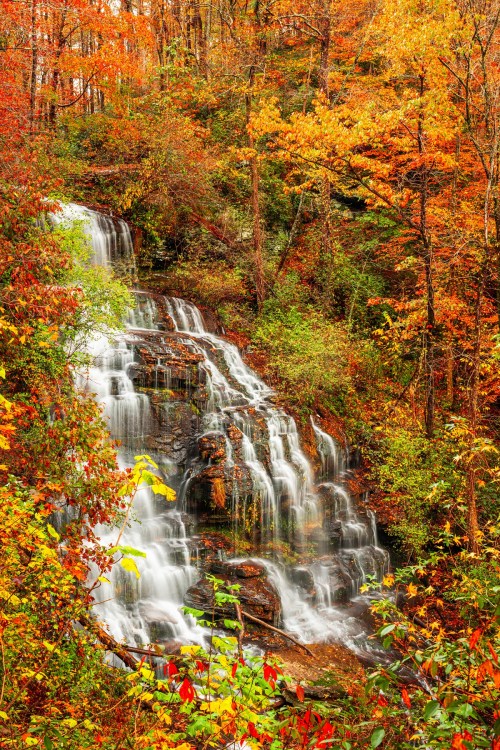 A cascading waterfall surrounded by vibrant autumn foliage in shades of orange, yellow, and green.