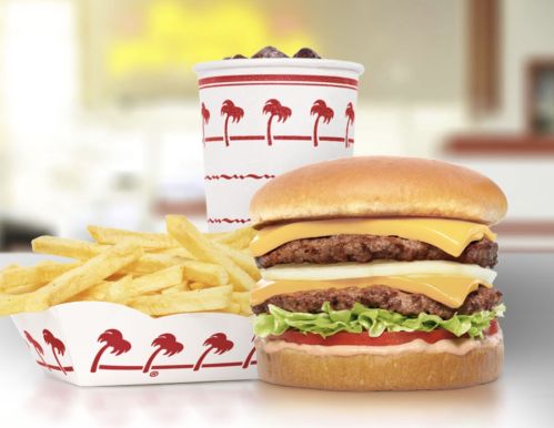 A double cheeseburger with lettuce and tomato, fries, and a drink in a red and white cup, set in a fast-food environment.