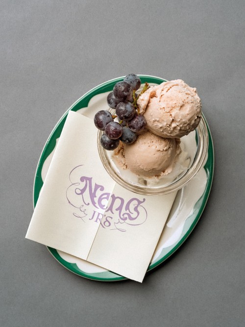 A glass dish with two scoops of peach ice cream, topped with grapes, on a green plate with two napkins.