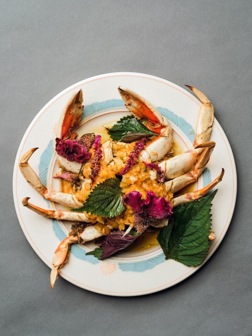 A beautifully plated crab dish garnished with vibrant flowers and green leaves on a decorative plate.
