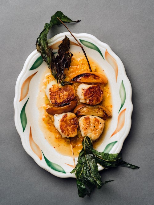 A plate of seared scallops with sautéed vegetables and greens, drizzled with a flavorful sauce.
