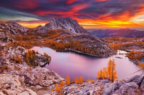 A stunning sunset over a mountain lake, surrounded by autumn foliage and dramatic rock formations.