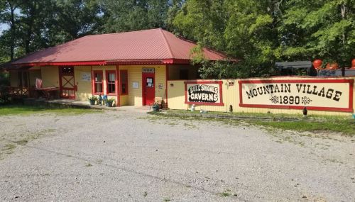 A yellow building with a red roof, labeled "Bull Shoals Caverns," surrounded by trees and gravel parking.