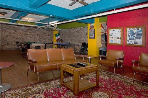 A cozy lounge area with brown leather chairs, a wooden coffee table, and colorful walls, featuring a pool table in the background.