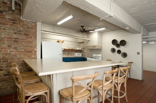 Modern kitchen with a brick wall, white countertops, blue cabinets, and a bar with wooden stools.
