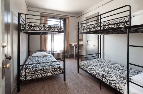 A simple room with two sets of black metal bunk beds and patterned bedding, featuring a window and a small table.