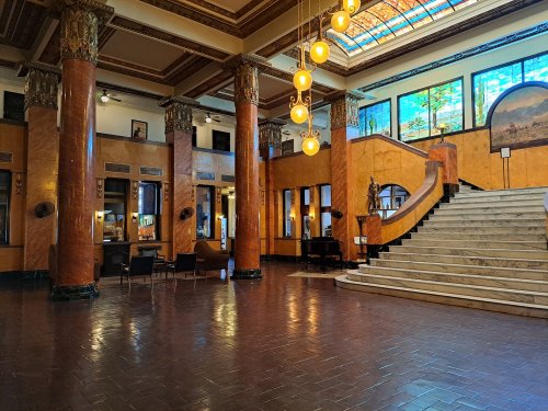 Interior of a grand hall featuring marble stairs, decorative columns, and large stained glass windows.