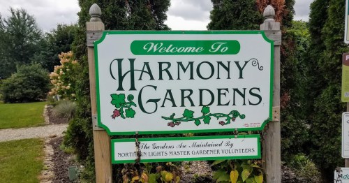 Sign for Harmony Gardens, featuring greenery and a welcoming message from Northern Lights Master Gardener Volunteers.