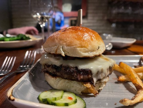 A juicy cheeseburger with melted cheese on a toasted bun, served with fries and a side of cucumber slices.