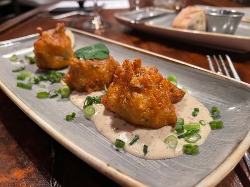 Three golden-brown fritters on a plate, garnished with green onions and served with a creamy sauce.